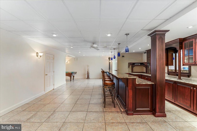 bar with decorative light fixtures, pool table, ornate columns, ceiling fan, and light stone counters