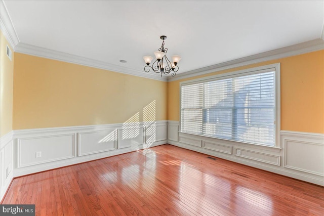 spare room featuring wood-type flooring, ornamental molding, and a chandelier