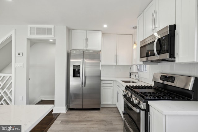 kitchen with white cabinetry, stainless steel appliances, sink, and light stone counters