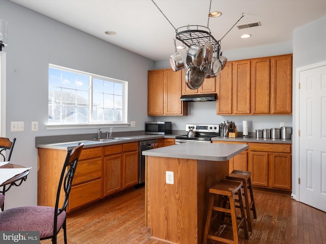 kitchen with a kitchen bar, sink, wood-type flooring, appliances with stainless steel finishes, and a kitchen island