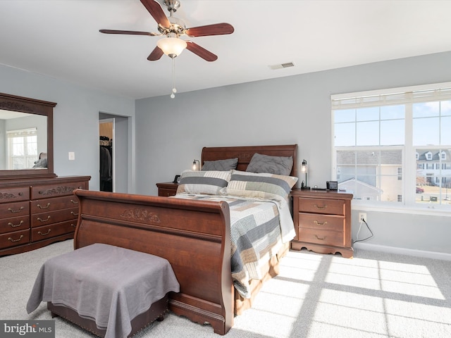 bedroom with a walk in closet, light colored carpet, ceiling fan, and a closet