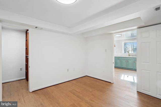 empty room featuring sink, light hardwood / wood-style flooring, and a raised ceiling