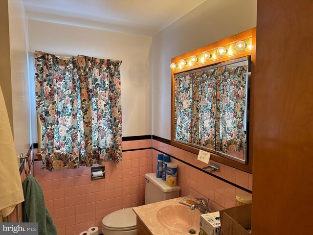 bathroom with toilet, vanity, and tile walls