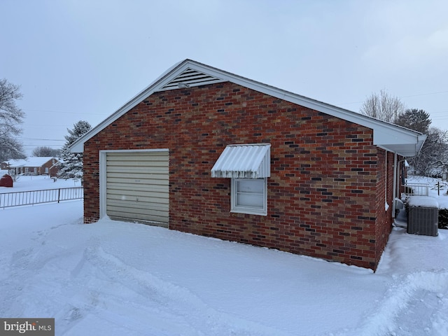 view of snow covered exterior with central AC and a garage