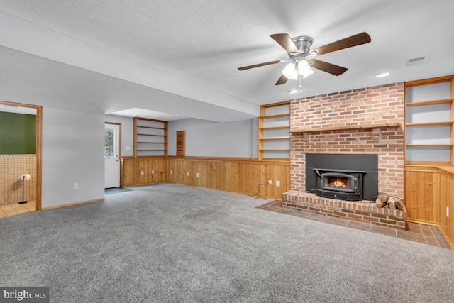 unfurnished living room featuring a fireplace, light colored carpet, a textured ceiling, and wooden walls