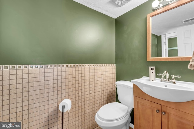 bathroom featuring toilet, a textured ceiling, tile walls, and vanity