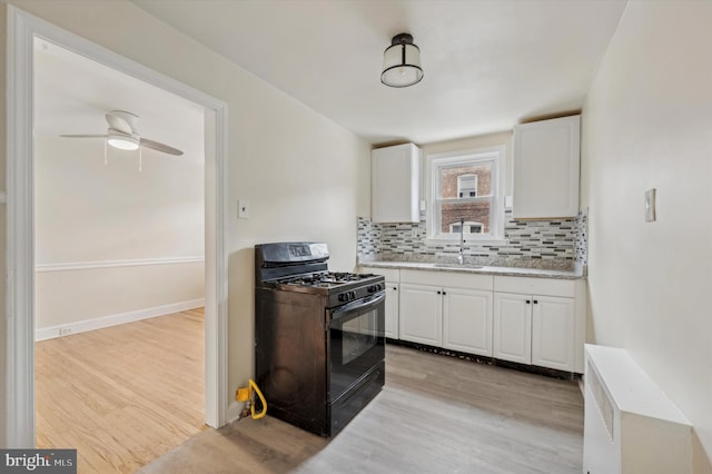 kitchen featuring white cabinets, decorative backsplash, black gas stove, light wood-type flooring, and ceiling fan