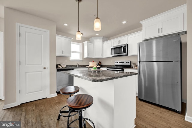 kitchen with a center island, hardwood / wood-style flooring, white cabinets, decorative light fixtures, and stainless steel appliances