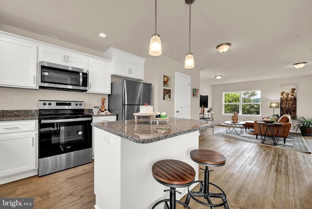 kitchen with appliances with stainless steel finishes, decorative light fixtures, white cabinetry, dark stone countertops, and a kitchen island