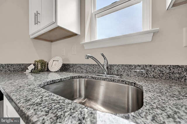 interior details featuring sink, white cabinetry, and stone countertops