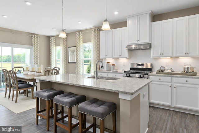 kitchen with pendant lighting, stainless steel range, white cabinetry, an island with sink, and sink