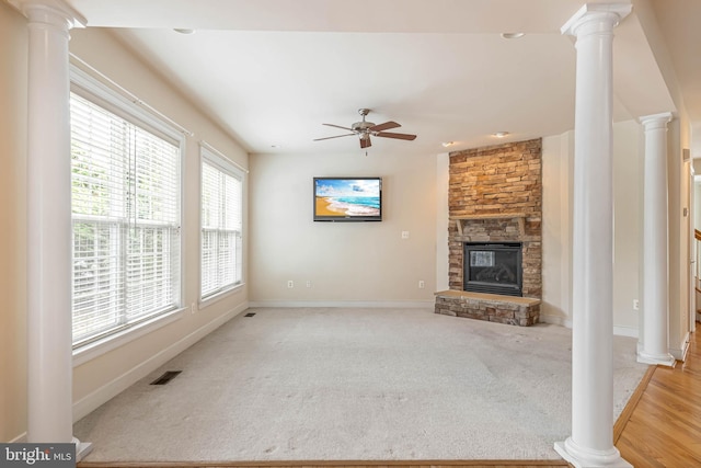 unfurnished living room featuring light carpet, ceiling fan, a fireplace, and ornate columns