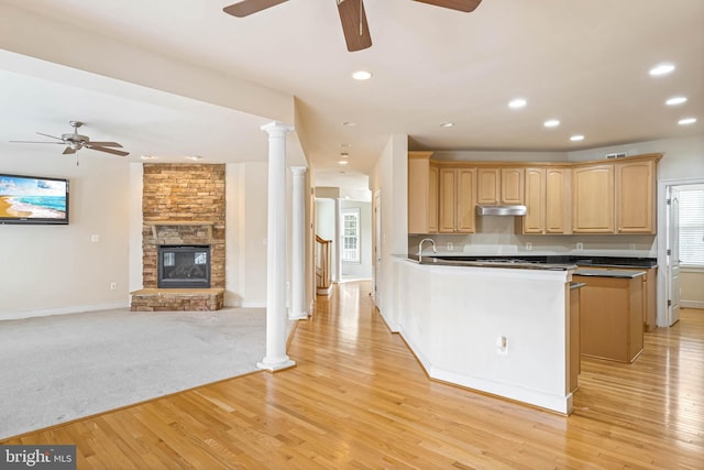 kitchen featuring a fireplace, light hardwood / wood-style floors, kitchen peninsula, light brown cabinets, and decorative columns