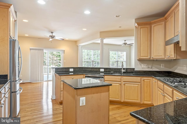 kitchen with kitchen peninsula, appliances with stainless steel finishes, a center island, dark stone counters, and sink