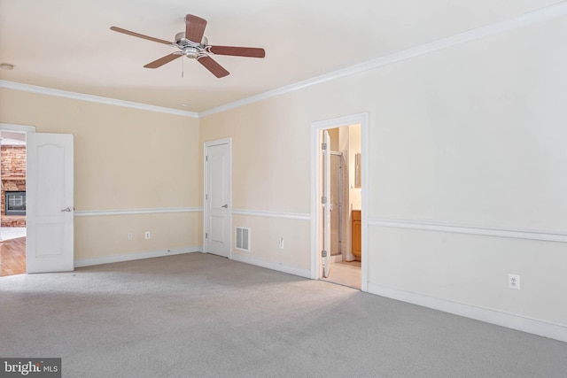 carpeted spare room featuring ceiling fan, a fireplace, and crown molding