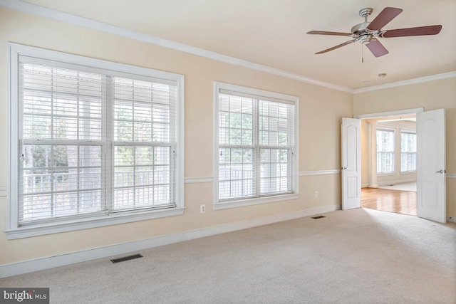 empty room featuring ceiling fan, plenty of natural light, light colored carpet, and crown molding