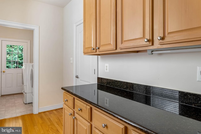 kitchen featuring washer / dryer, dark stone countertops, and light hardwood / wood-style floors