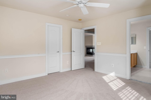 unfurnished bedroom with ceiling fan, ensuite bath, light carpet, and a multi sided fireplace