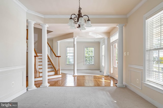 carpeted foyer entrance with plenty of natural light, crown molding, ornate columns, and an inviting chandelier