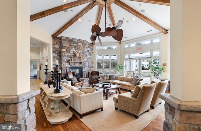 living room with light wood-type flooring, beamed ceiling, a fireplace, and high vaulted ceiling