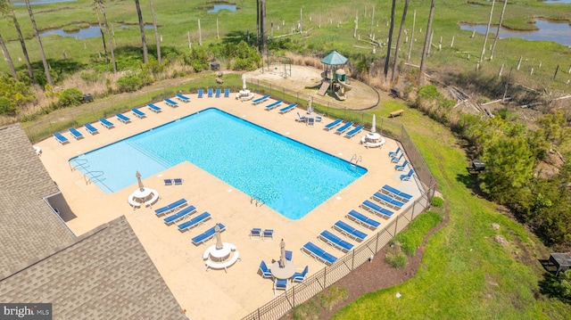 view of swimming pool with a playground, a patio area, and a water view