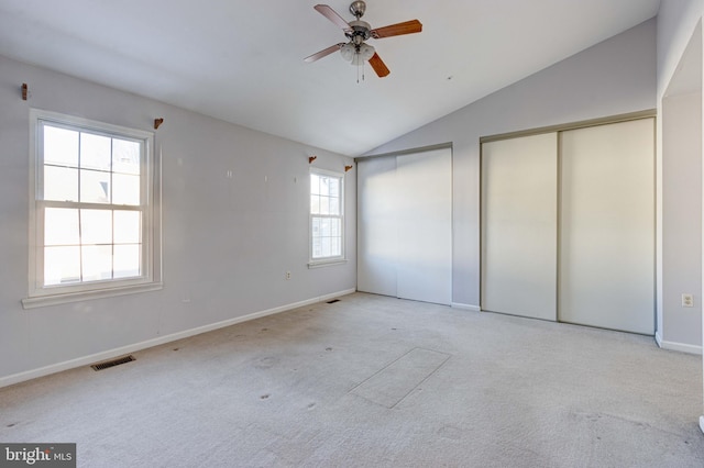 unfurnished bedroom with light carpet, multiple closets, vaulted ceiling, and ceiling fan