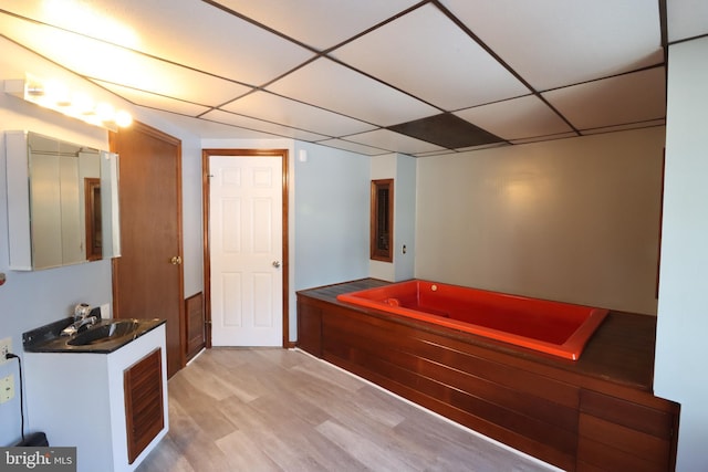 bathroom featuring wood-type flooring, a washtub, a drop ceiling, and vanity