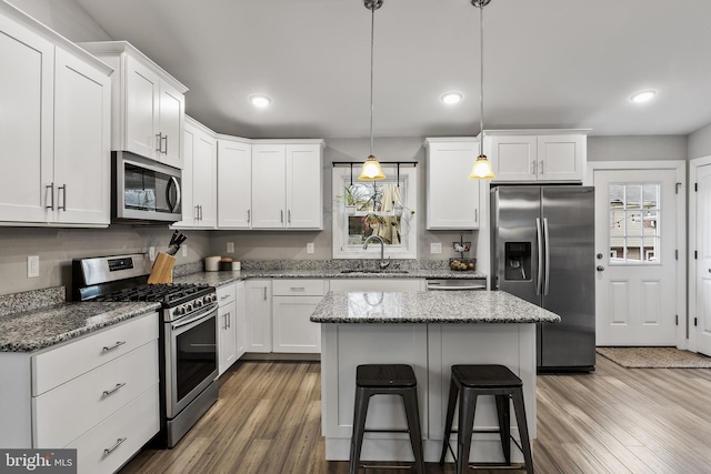 kitchen with hanging light fixtures, stainless steel appliances, white cabinets, a kitchen island, and dark stone counters