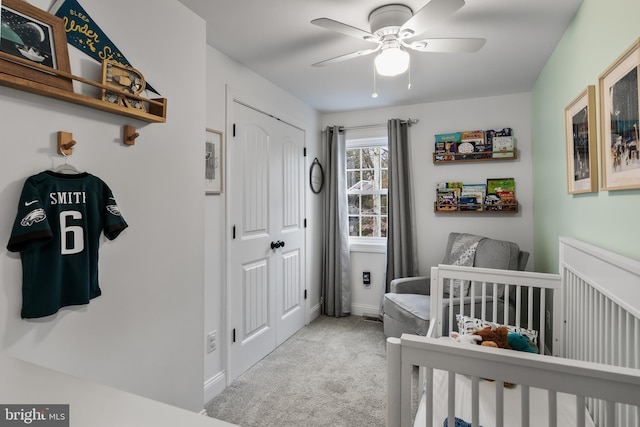 bedroom featuring a nursery area, light colored carpet, ceiling fan, and a closet