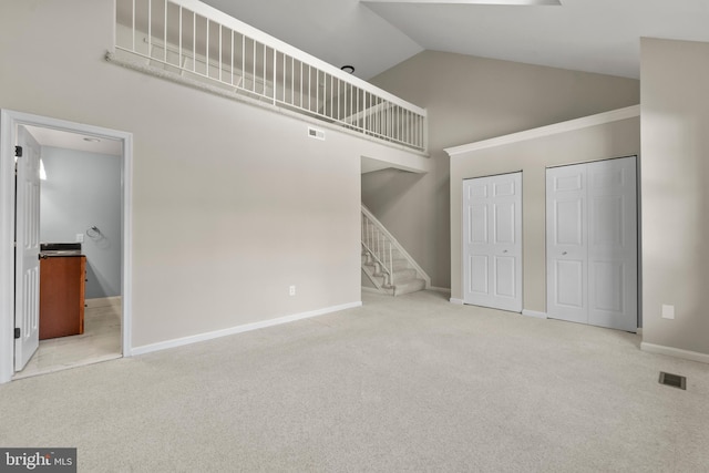 unfurnished bedroom featuring high vaulted ceiling, light carpet, and multiple closets