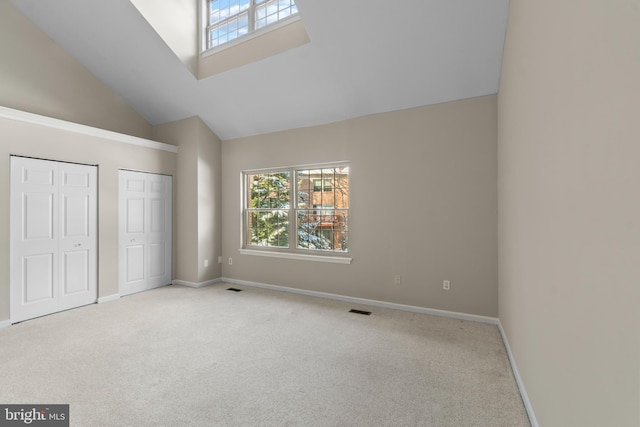 unfurnished bedroom with light carpet, multiple closets, multiple windows, and high vaulted ceiling