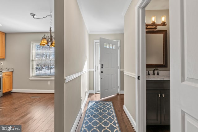 entrance foyer with dark wood-type flooring, crown molding, an inviting chandelier, and sink