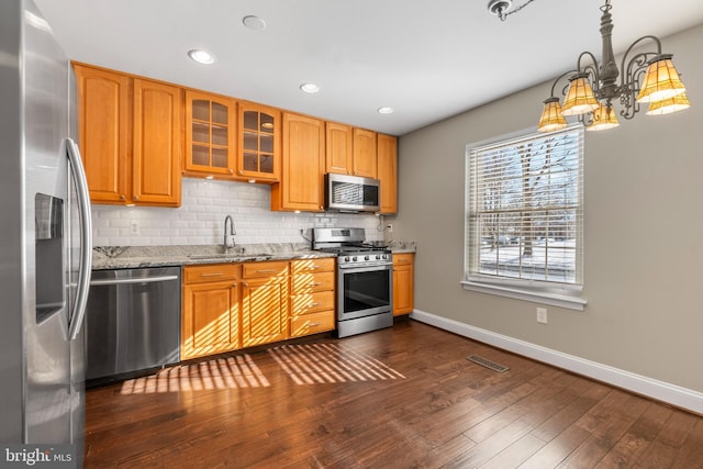 kitchen featuring light stone countertops, appliances with stainless steel finishes, dark hardwood / wood-style flooring, sink, and backsplash