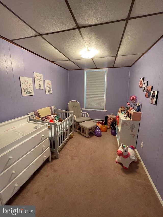 carpeted bedroom featuring a drop ceiling and a crib