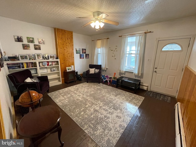 living area with ceiling fan, a baseboard heating unit, dark hardwood / wood-style flooring, and a textured ceiling