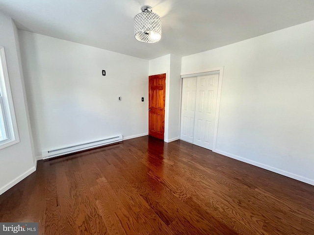 unfurnished bedroom featuring a baseboard heating unit, a closet, and dark hardwood / wood-style floors