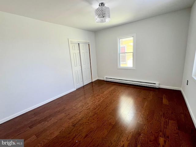 unfurnished bedroom featuring a baseboard heating unit, dark wood-type flooring, and a closet