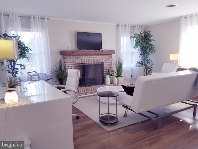 living room with a brick fireplace, plenty of natural light, wood-type flooring, and crown molding