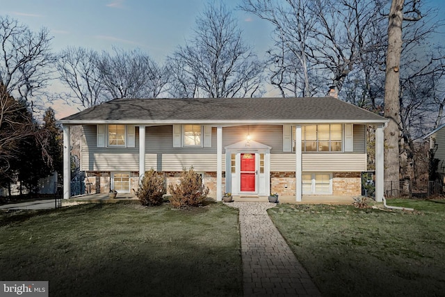 split foyer home with a front yard, brick siding, roof with shingles, and a chimney