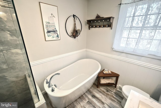 full bath with a soaking tub, wood finished floors, wainscoting, and toilet