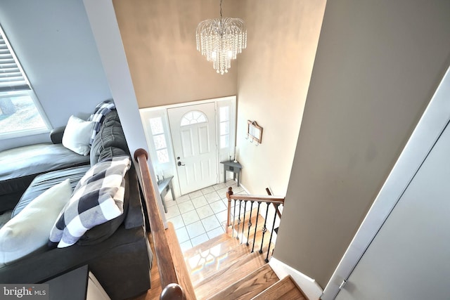 foyer featuring tile patterned flooring, a chandelier, a high ceiling, and baseboards