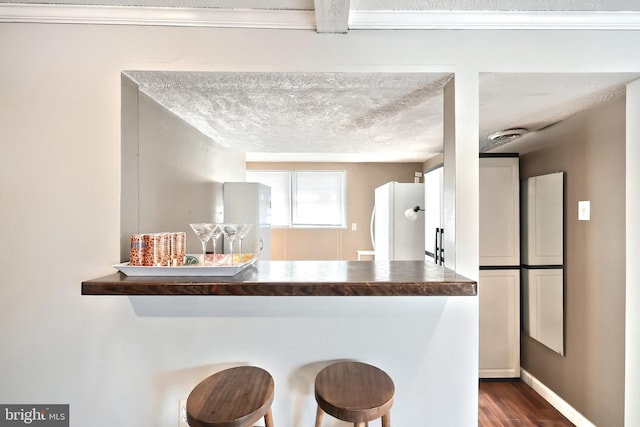 kitchen with a kitchen bar, dark wood-type flooring, a textured ceiling, freestanding refrigerator, and baseboards