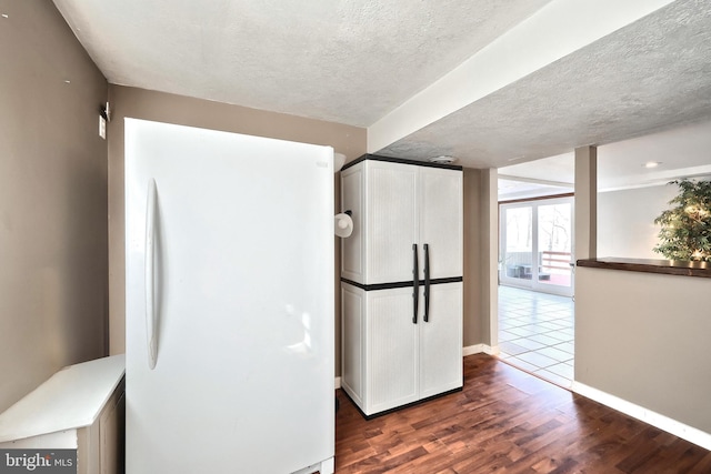 kitchen with dark wood-type flooring, a textured ceiling, freestanding refrigerator, white cabinets, and baseboards