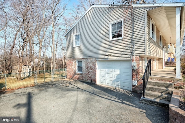 view of side of home with a gate, an attached garage, fence, and brick siding