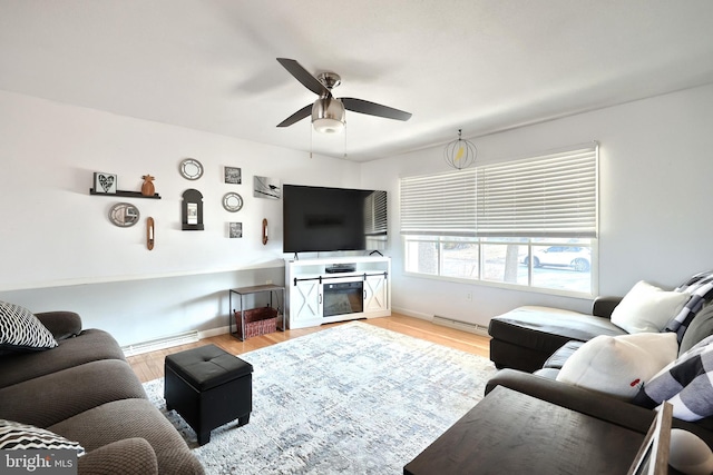 living area with baseboards, baseboard heating, a ceiling fan, and light wood-style floors