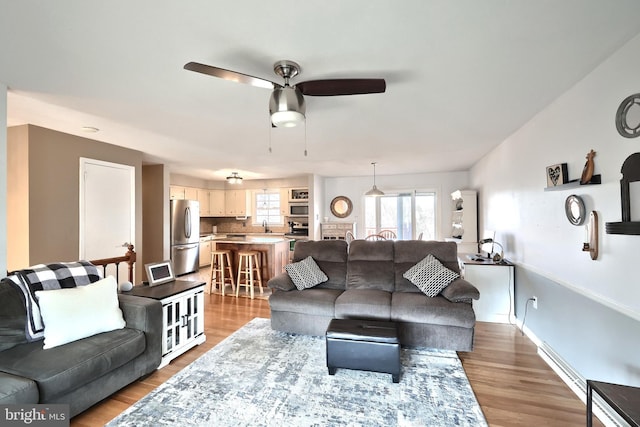 living area featuring baseboards, a ceiling fan, and light wood finished floors