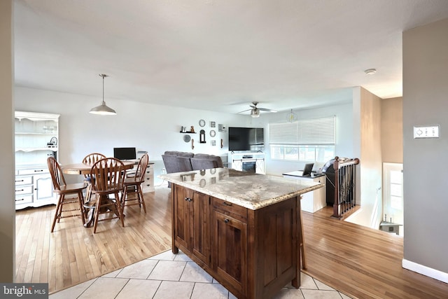 kitchen featuring light wood finished floors, a kitchen island, ceiling fan, decorative light fixtures, and light stone counters