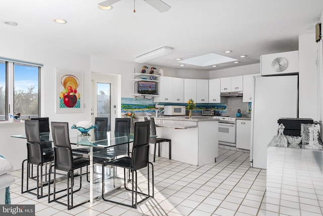 kitchen featuring a kitchen island, tasteful backsplash, white cabinetry, light tile patterned floors, and white appliances