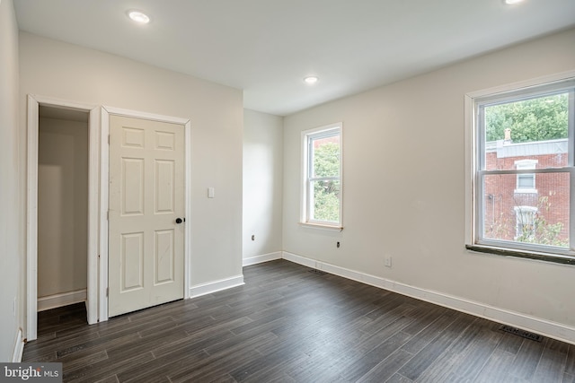 unfurnished bedroom with a closet, multiple windows, and dark wood-type flooring