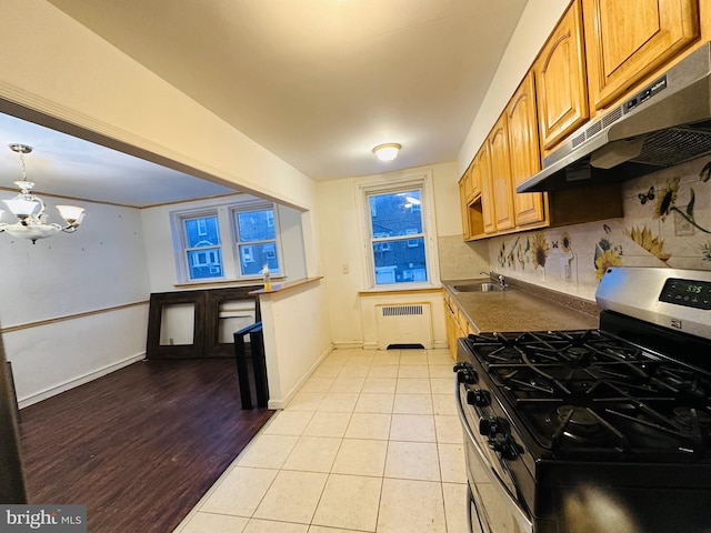 kitchen with light tile patterned floors, radiator heating unit, a notable chandelier, stainless steel gas stove, and sink